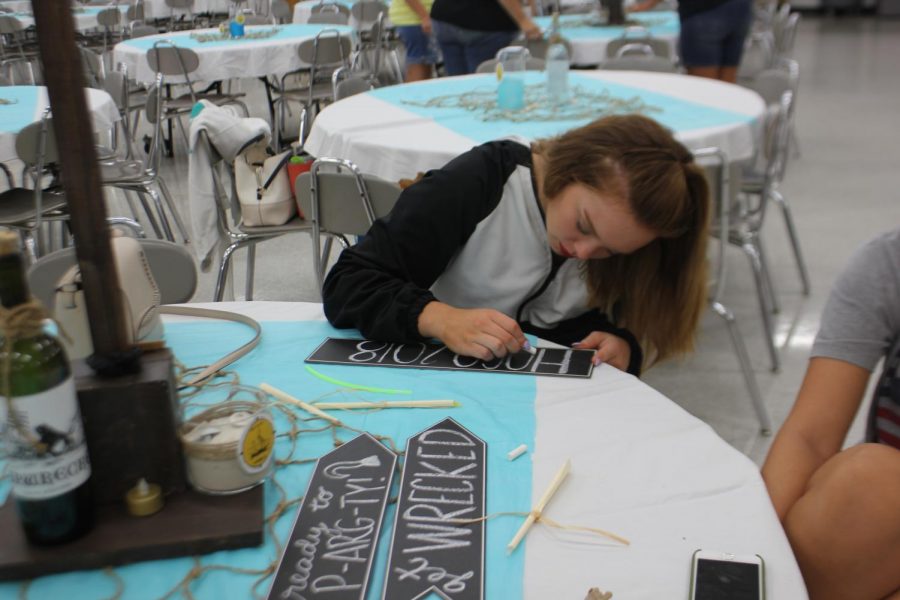 Creativity. Writing on a chalkboard sign for the photo booth, Senior Prowler Hayden Foster helps set up for the dance.  People all night long would take pictures with the ship replica photo booth at homecoming.